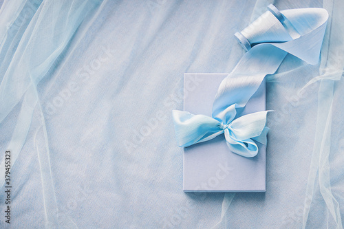 Gift boxes with hand dyed silk ribbon with bow on wood spool on blue fabric with folds background and copy space © AnaGost