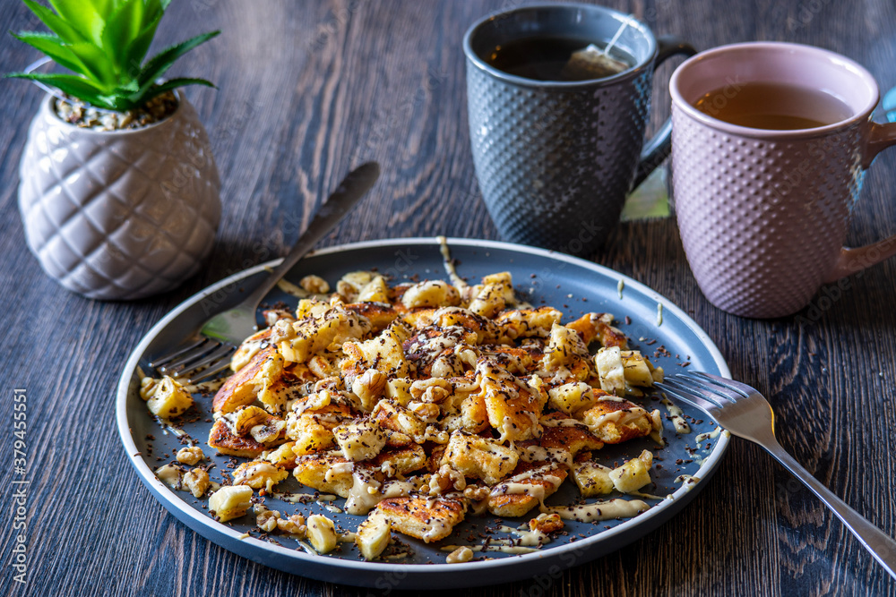 Fluffy, gluten-free, shredded pancake / kaiserschmarrn served with halvah spread, banana, walnuts, and grated chocolate placed on a decorative plate and teacups at the background