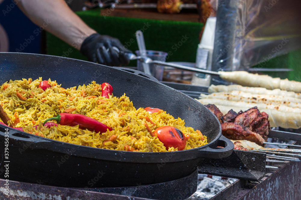 Healthy street food to go - in a large cauldron hot pilaf with pieces of meat and whole hot red pepper. Delicious food cooked over an open fire, which is offered at a street food fair, event, festival