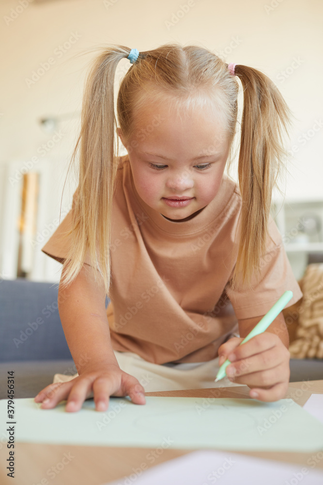 Vertical portrait of cute blonde girl with down syndrome drawing or writing during development exercises at home Vertical portrait of cute blonde girl with down syndrome drawing or writing during development exercises at home