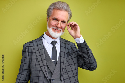 portrait of pleasant senior businessman in stylish suit isolated in studio, green background. gray bearded male is successful enrepreneur, posing photo