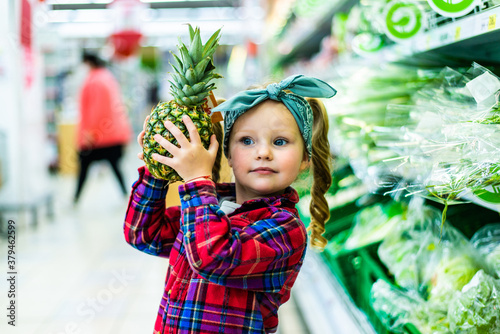 Cute little girl holding a pineapple in a food store or supermarket