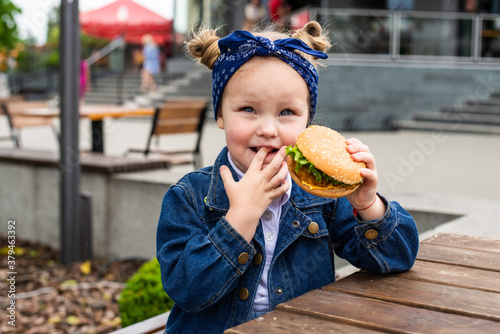Little cute girl eating a burger in a cafe. Concept of a children's fast food meal