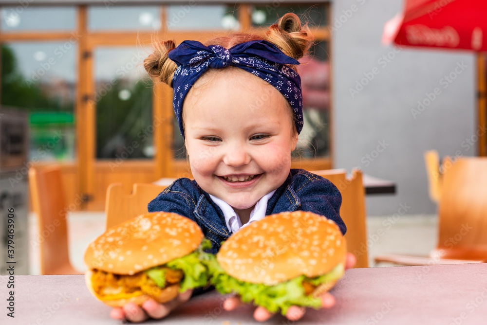 Cute little girl holding two burgers in hands in fast food cafe Cute little girl holding two burgers in hands in fast food cafe