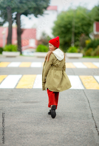A girl in ordinary autumn clothes on a city street walks on the asphalt