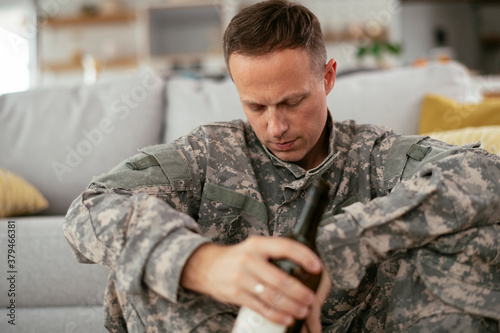 Depressed soldier with bottle sitting in livig room., Alcohol addiction.