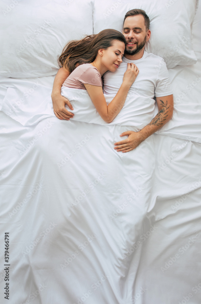Bedtime. The family are sleeping. Beautiful young couple in love are lying on the big white bed and resting. Husband and wife together in bed. Top view photo