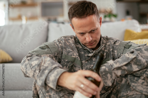 Depressed soldier with bottle sitting in livig room., Alcohol addiction.