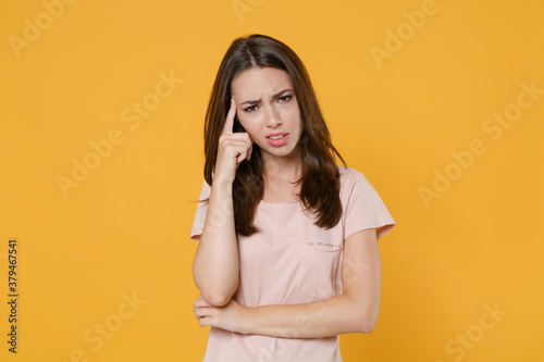 Displeased upset worried tired young brunette woman wearing pastel pink casual t-shirt standing posing put hand on head looking camera isolated on bright yellow color wall background studio portrait.