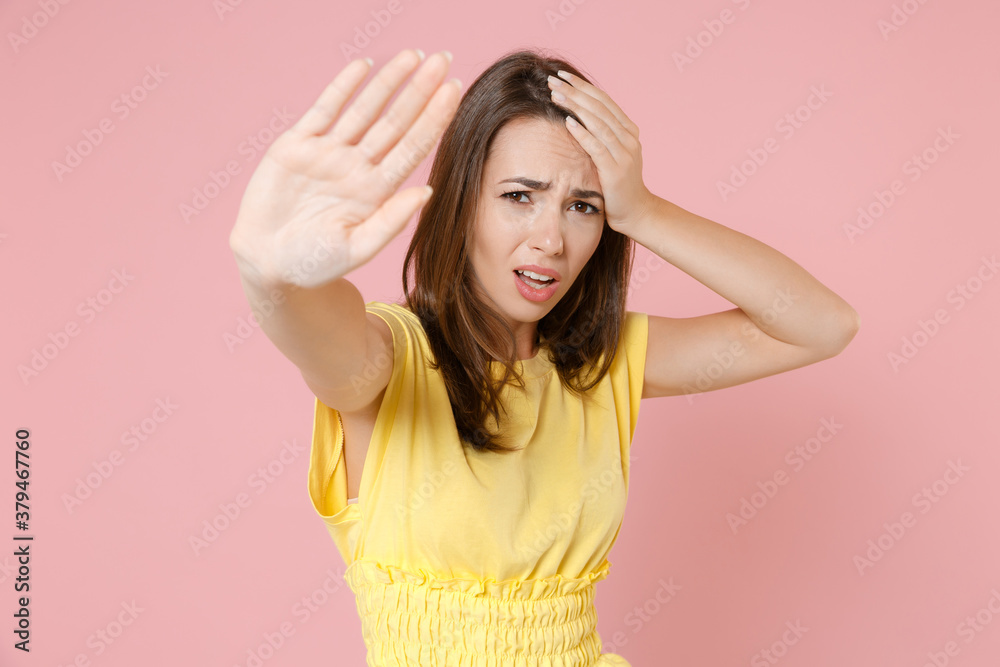 Displeased worried dissatisfied young brunette woman wearing yellow casual t-shirt posing standing showing stop gesture with palm put hand on head isolated on pastel pink background studio portrait. Displeased worried dissatisfied young brunette woman wearing yellow casual t-shirt posing standing showing stop gesture with palm put hand on head isolated on pastel pink background studio portrait.