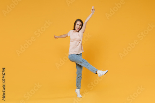 Full length portrait of funny surprised cheerful young woman 20s in pastel pink casual t-shirt posing dancing rising spreading hands and legs looking camera isolated on yellow color background studio. © ViDi Studio