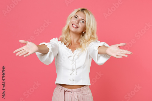 Smiling joyful beautiful attractive young blonde woman 20s wearing white casual clothes standing reach out stretch hands looking camera isolated on bright pink colour background studio portrait.