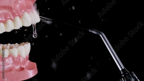 Water flosser cleaning jaw with white teeth at the distance on black background. Using oral irrigator, dental health. Everyday hygiene, mouth washing in slow motion. Full HD 240 fps photo