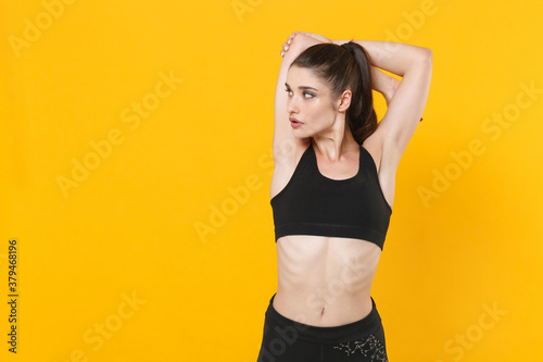 Strong young fitness sporty woman 20s wearing black sportswear posing working out training doing stretching exercising looking aside isolated on bright yellow color wall background studio portrait. © ViDi Studio