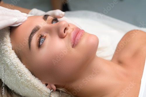 Young woman in a beauty salon. The beautician makes a facial cleansing procedure.