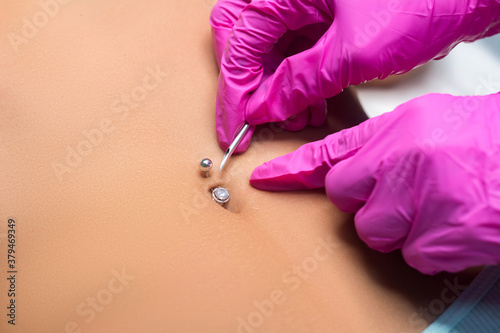 Belly button piercing. The beautician does the piercing procedure. photo