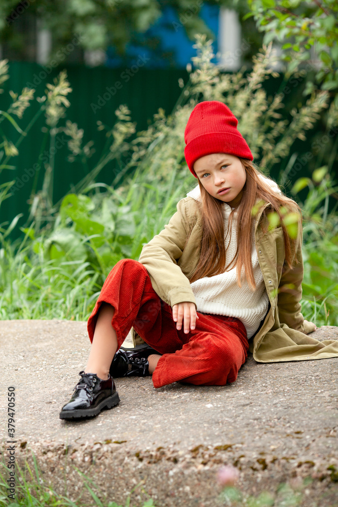 Girl in autumn clothes sits cross-legged on a concrete block Girl in autumn clothes sits cross-legged on a concrete block