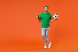 Full length portrait funny young man football fan in green t-shirt cheer up support favorite team with soccer ball hold beer bottle isolated on orange background studio. People sport leisure concept.