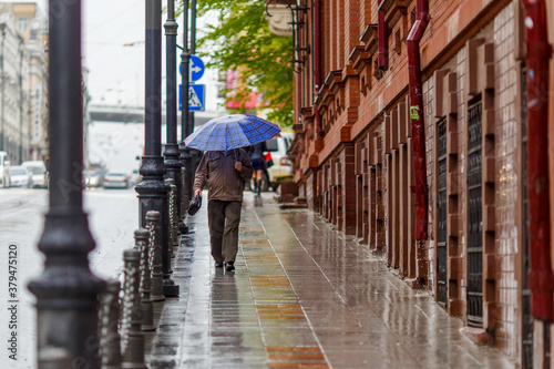 A man walks under an umbrella during the rain, having his face off the camera