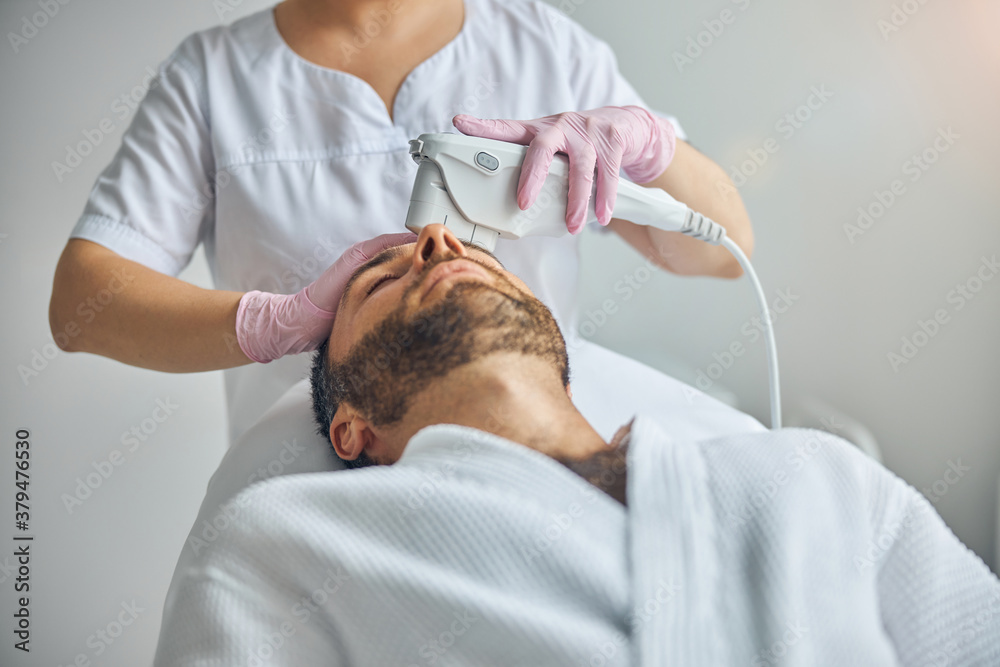 Female beautician treating male skin with laser device Female beautician treating male skin with laser device