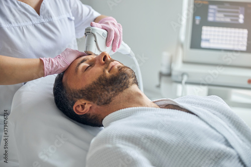 Doctor beautician treating male skin with laser device