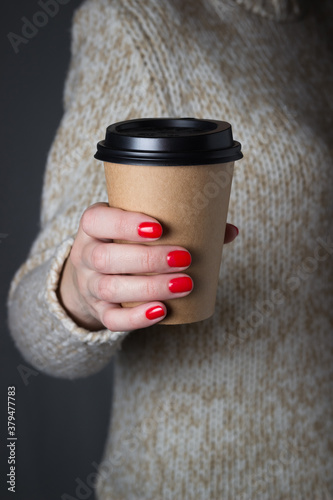 Young woman holding in hands blank take away kraft coffee cup. Light sweater.