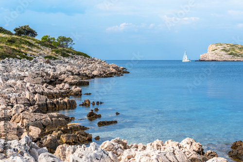 The rocky shore of the island of Lavsa, Croatia, and the yacht going to the sea photo