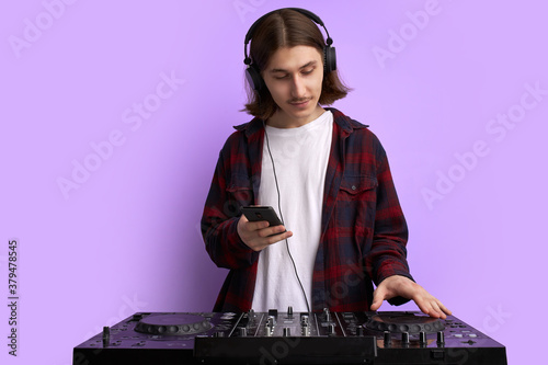 modern club DJ playing mixing music on vinyl turntable, isolated in studio. caucsaian male perform techno style music, enjoy playing on equipment, use smartphone