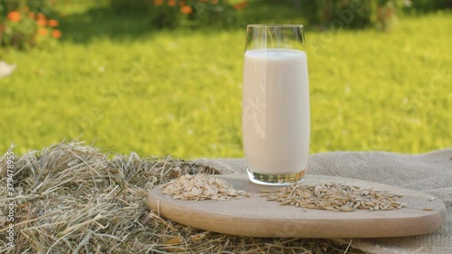 Close up oat milk in a glass. Oat grains and oatmeal on a wooden cutting board. Fresh hay, jute burlap, rural still life. The camera moves slowly on the slider