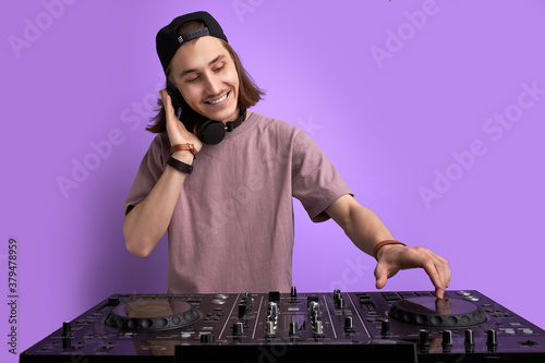 positive male DJ playing music on purple background, caucasian long haired man in casual wear perform club music, wearing headphones