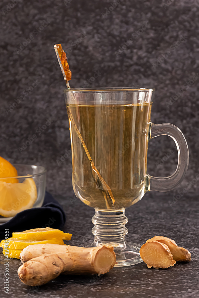 A glass of hot ginger and lemon tea with slices of lemon and ginger root on dark background A glass of hot ginger and lemon tea with slices of lemon and ginger root on dark background