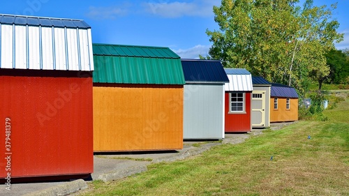Colorful wooden sheds in a row. American shed is typically a simple, single-story roofed structure in a back garden or on an allotment that is used for storage, hobbies, or as a workshop. 