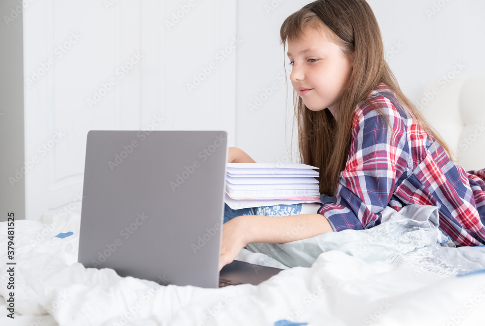Distance learning online education. Schoolgirl studying at home with digital laptop notebook and doing school homework lying on bed at home. Distance learning online education. Schoolgirl studying at home with digital laptop notebook and doing school homework lying on bed at home.