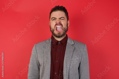 Young caucasian businessman wearing casual clothes standing over isolated red background sticking tongue out happy with funny expression. Emotion concept. © Roquillo