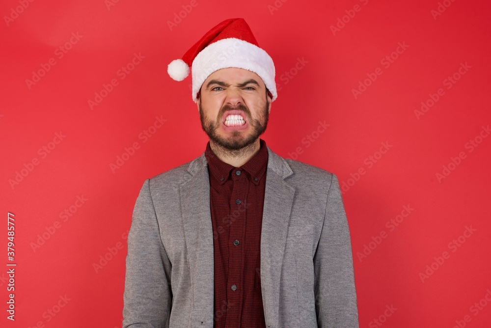 Young caucasian businessman wearing casual clothes standing over isolated red background, keeps teeth clenched, frowns face in dissatisfaction, irritated because of much duties. Young caucasian businessman wearing casual clothes standing over isolated red background, keeps teeth clenched, frowns face in dissatisfaction, irritated because of much duties.