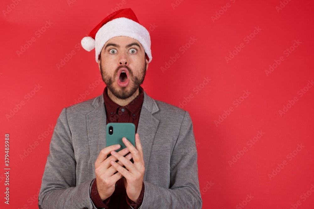 Shocked Young caucasian businessman wearing casual clothes standing over isolated red background opens mouth hold phone reading advert unbelievable big shopping prices Shocked Young caucasian businessman wearing casual clothes standing over isolated red background opens mouth hold phone reading advert unbelievable big shopping prices