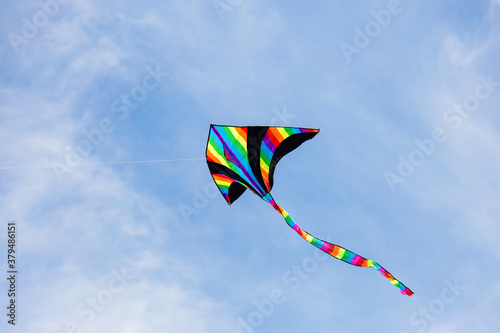 Colorful kite flying in the cloudy sky. Bright multicolored kite on a background of white clouds and blue sky