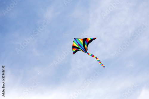 Colorful kite flying in the cloudy sky. Bright multicolored kite on a background of white clouds and blue sky