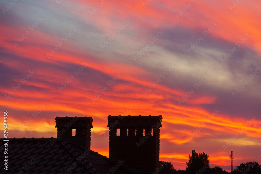 Fototapeta premium Golden sunset. Only the silhouettes of the houses are visible in orange sky. Orange evening sunset sky above house roof with small suburban houses at horizontal line.