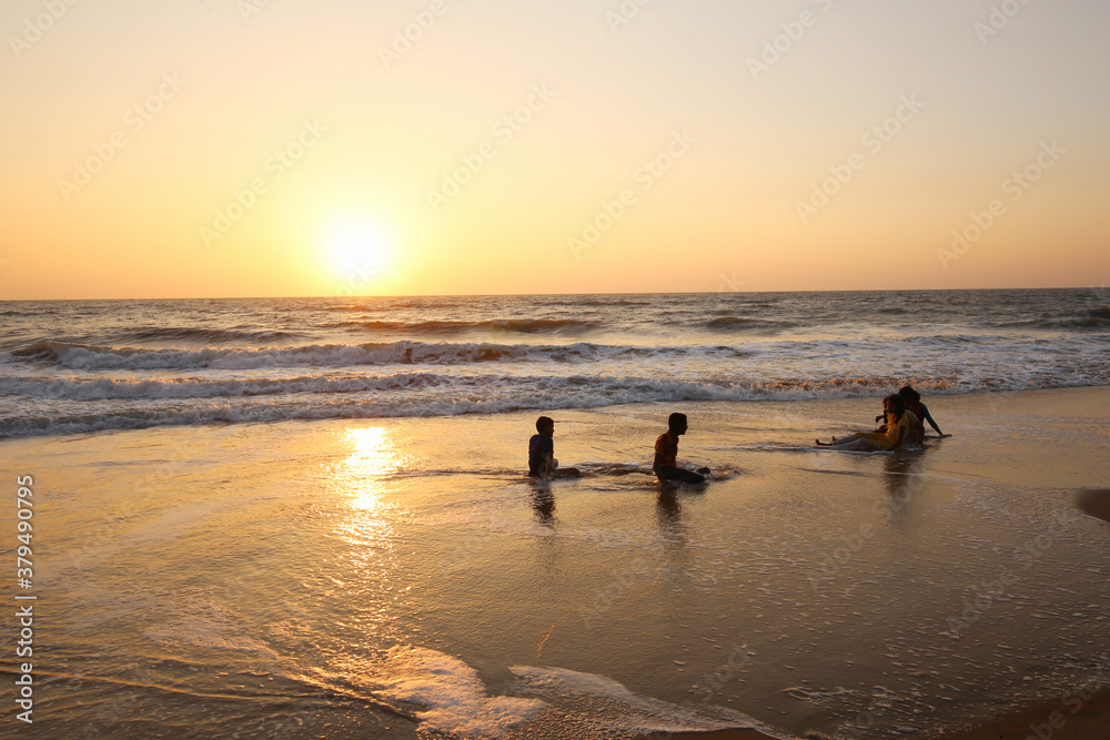 Awe scene with Silhouettes Teenagers  on Nirvana beach at South India. Orange sunrise (sunset).    ( unrecognizable persons)