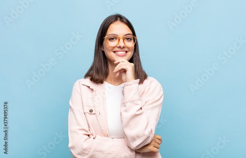 young pretty woman looking happy and smiling with hand on chin, wondering or asking a question, comparing options