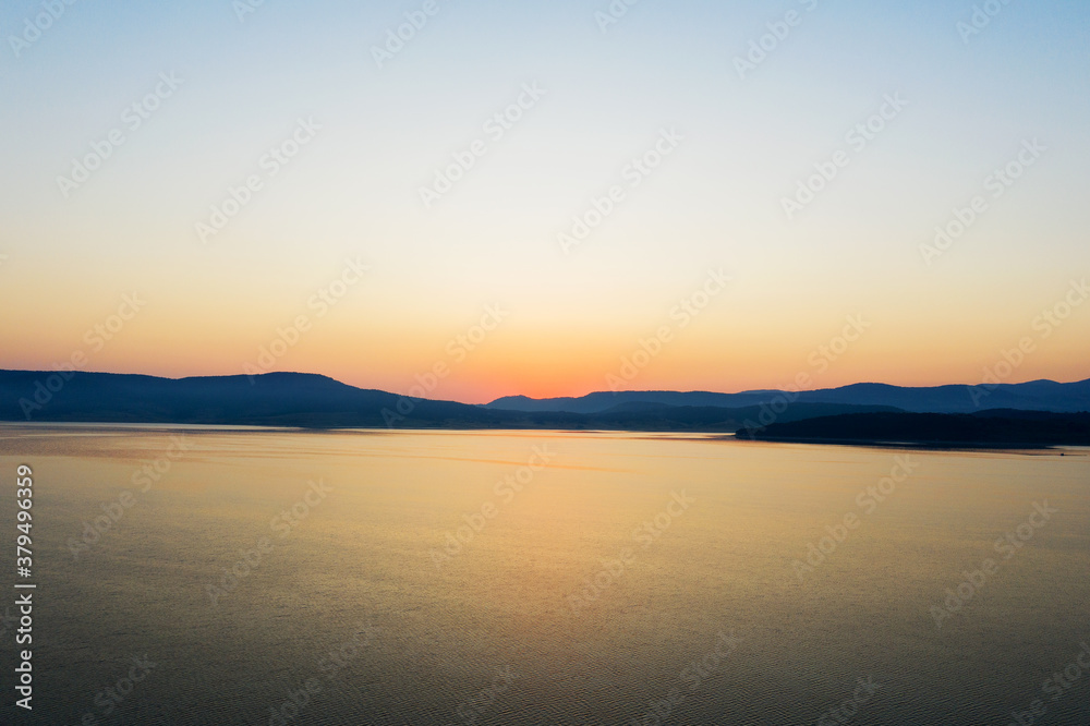 Beautiful authentic landscape of rising sun over lake, silhouettes of mountains, aerial view from the drone. Batak reservoir located in Rhodope Mountains, Bulgaria. Attracts many tourists. Travel 