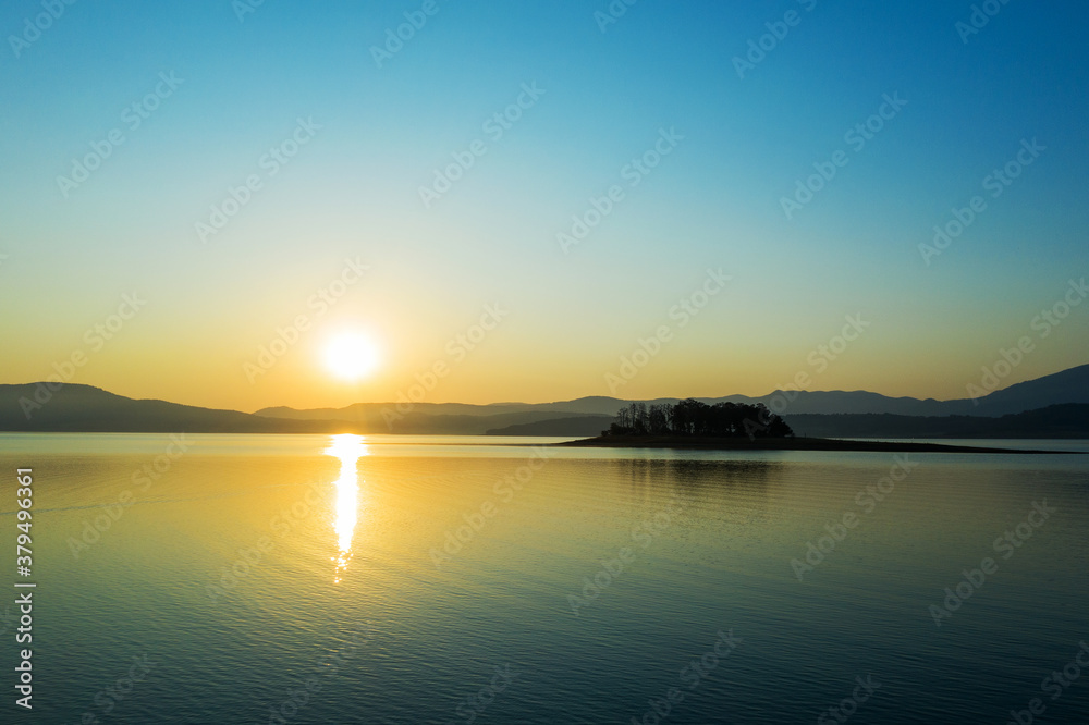 Beautiful authentic landscape of rising sun over lake, silhouettes of mountains, aerial view from drone. Batak reservoir located in Rhodope Mountains, Bulgaria. Attracts many tourists. Travel 