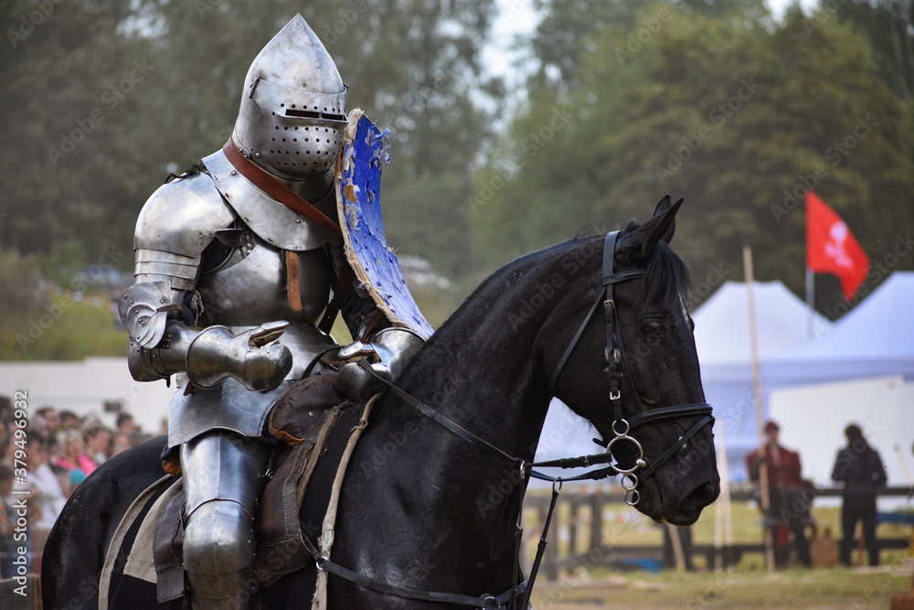 Knight with blue shield on a black horse after jousting at Late Middle Ages Tournament reenactment Knight with blue shield on a black horse after jousting at Late Middle Ages Tournament reenactment