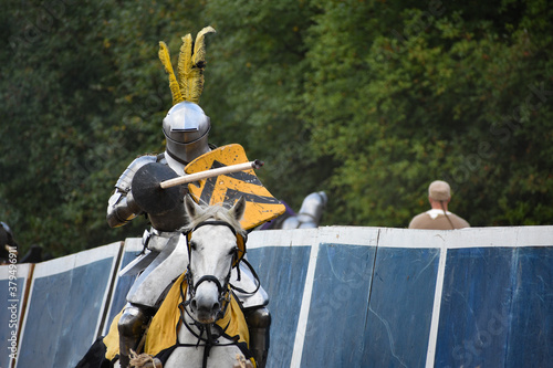 Knight with lance and black-and-yellow shield on a running white horse during jousting at Late Middle Ages Tournament reenactment