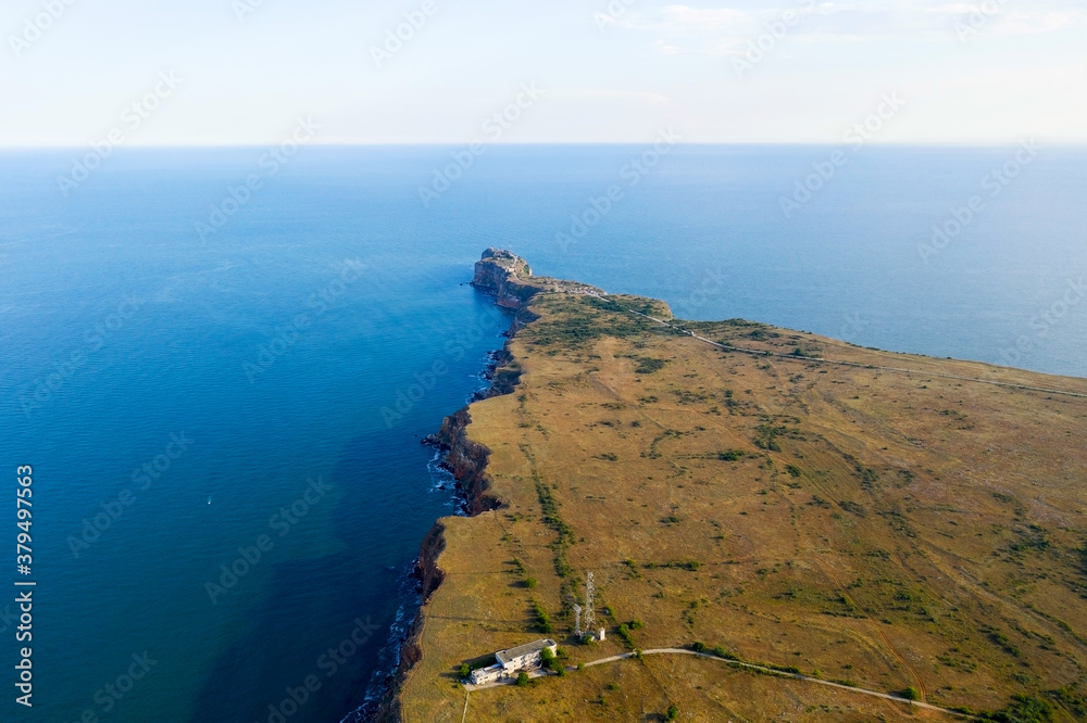Narrow, long cape Kaliakra goes into sea on northern coast of Bulgaria. High steep banks of reddish hue are in harmony with greenery of grass and endless blue sea. View from drone.