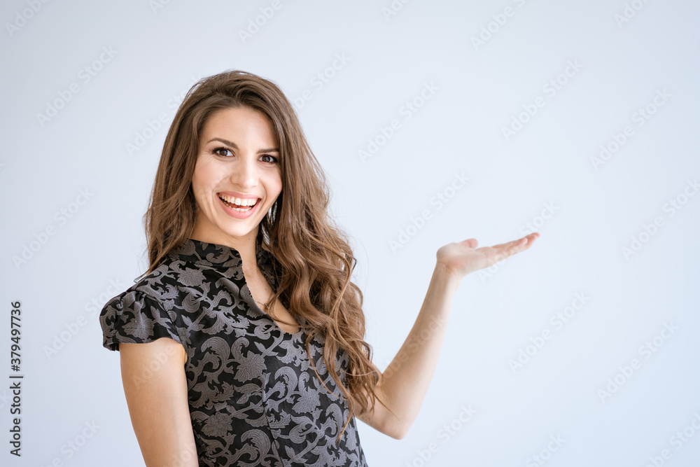 A young beautiful woman smiles on a white background and points to the side