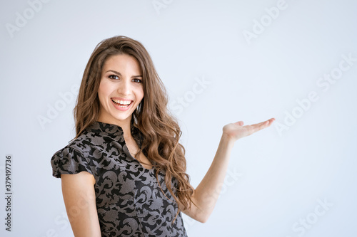 A young beautiful woman smiles on a white background and points to the side