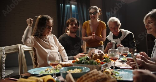 Large caucasian family celebrating thanksgiving day waiting for little girl to put her fork in fresh roasted turkey. Little kid happy during celebration 4k footage photo