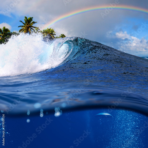 Perfect tropical ocean view splitted by waterline to two part. Shorebreak breaking surfing wave. Palms and clouds in daylight with colorful rainbow.